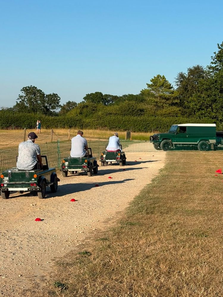 Three adults driving mini Land Rovers in single file down the gravel track in evening sunshine